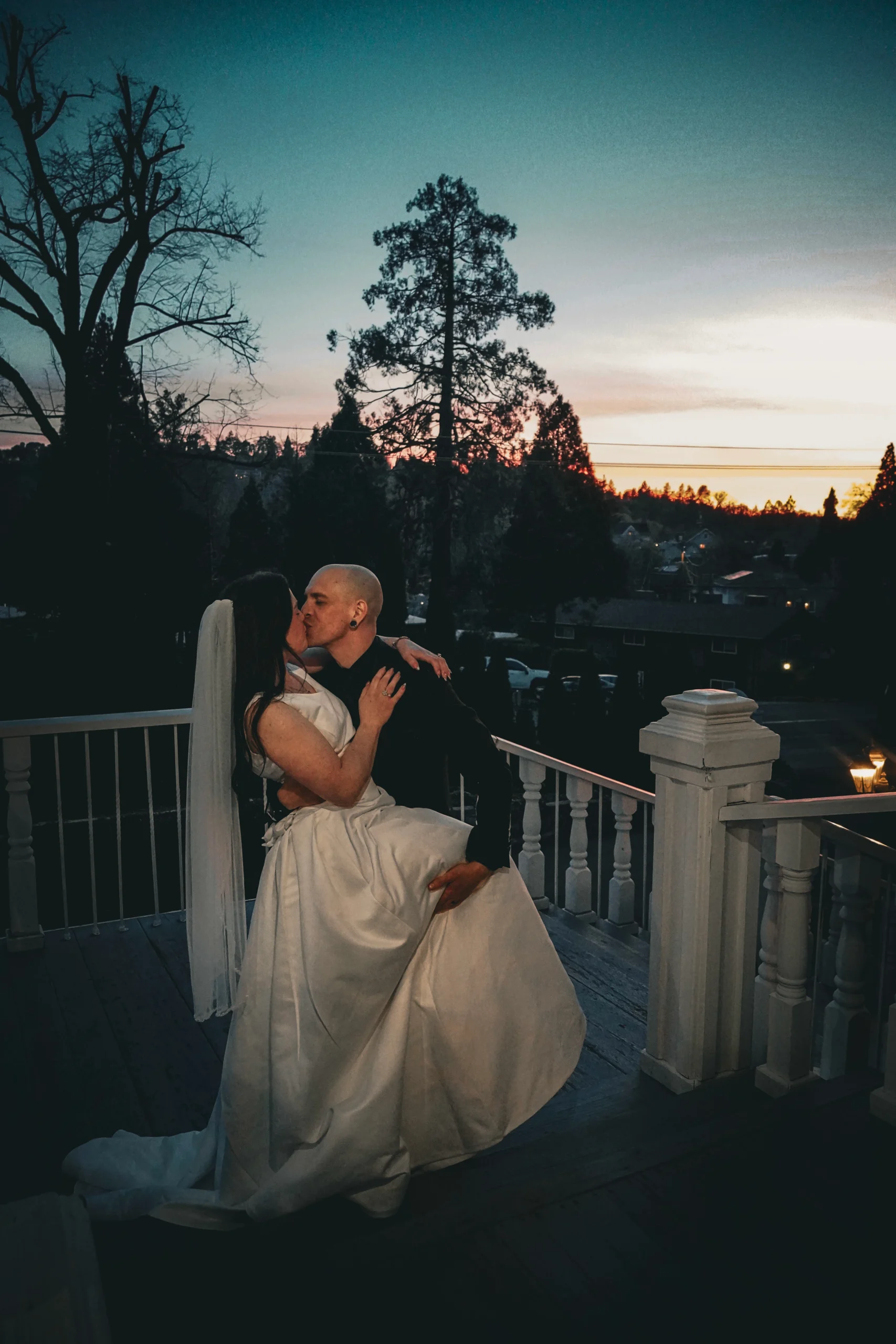 A groom holds his brides leg while he kisses her under a magical sunset on the evening of their wedding in Northern California