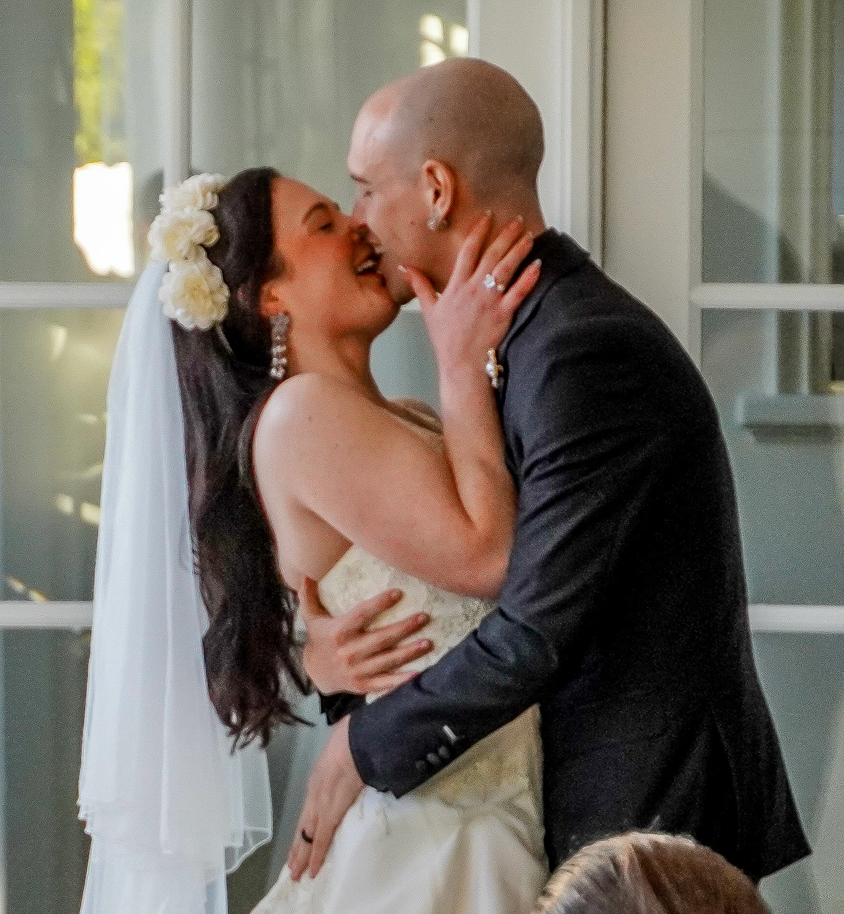 A close up of the bride and grooms first kiss as husband and wife. The bride shows off her ring and princess nails. They both smile while kissing. It's a very loving moment.